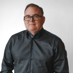 jim-willson A person wearing glasses and a dark button-up shirt stands against a plain white background, exuding the precision and creativity often seen in home designers.
