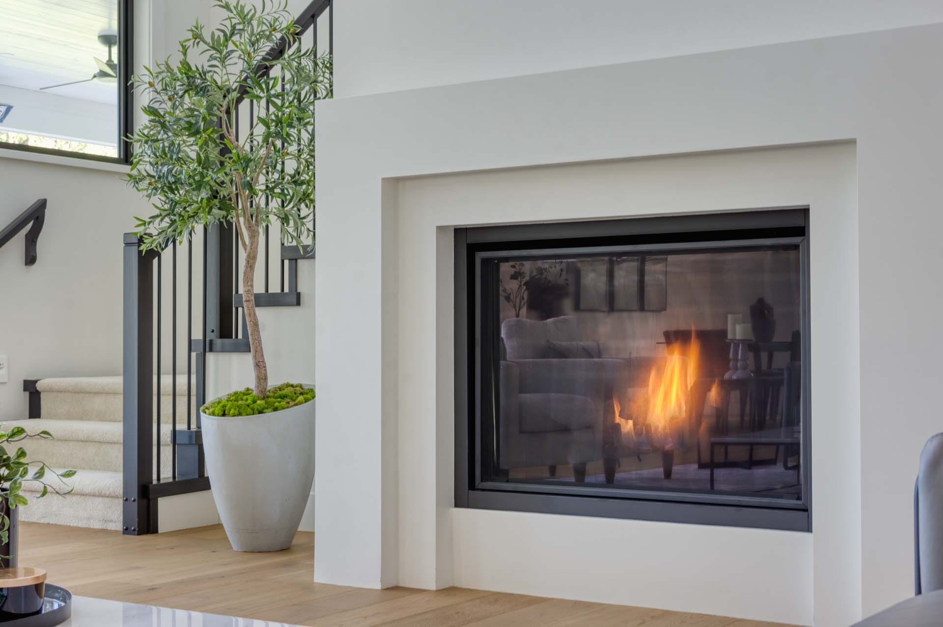 Modern living room with a lit fireplace, a potted plant, and a staircase thoughtfully crafted by skilled home designers.